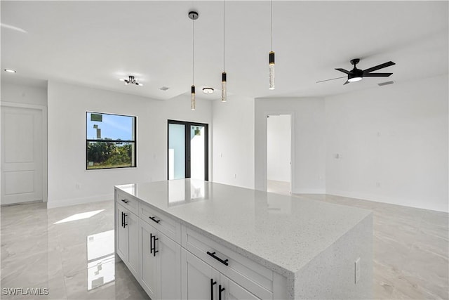 kitchen with light stone countertops, a center island, white cabinetry, hanging light fixtures, and ceiling fan