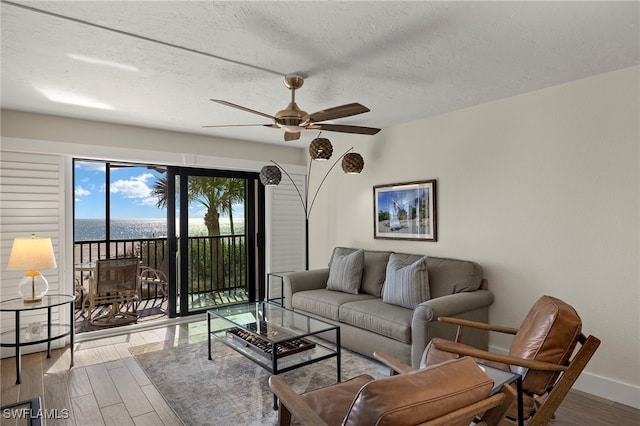 living room featuring ceiling fan, a water view, and a textured ceiling