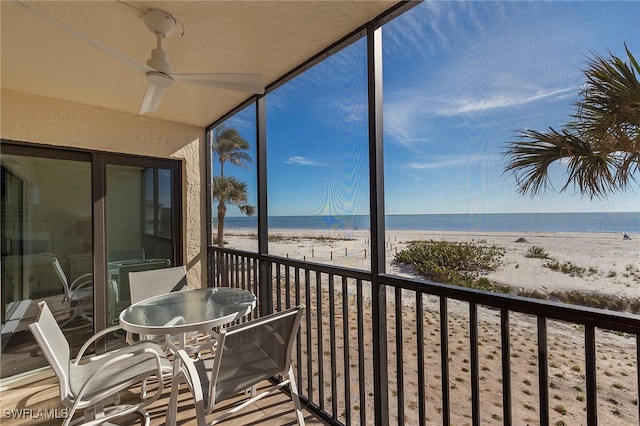 sunroom featuring ceiling fan, a water view, and a view of the beach