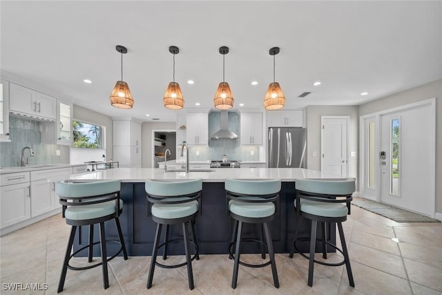 kitchen with light countertops, freestanding refrigerator, light tile patterned flooring, white cabinetry, and wall chimney exhaust hood