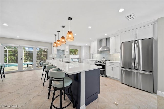 kitchen featuring stainless steel appliances, a sink, visible vents, white cabinetry, and wall chimney exhaust hood