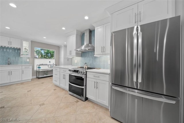 kitchen featuring light countertops, decorative backsplash, appliances with stainless steel finishes, white cabinets, and wall chimney exhaust hood