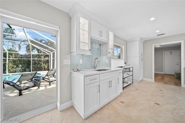 kitchen featuring light countertops, decorative backsplash, glass insert cabinets, white cabinets, and a sink