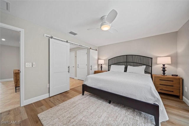 bedroom featuring visible vents, light wood-style flooring, baseboards, and a barn door