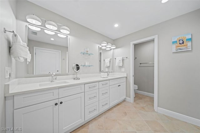 bathroom featuring baseboards, a sink, toilet, and double vanity