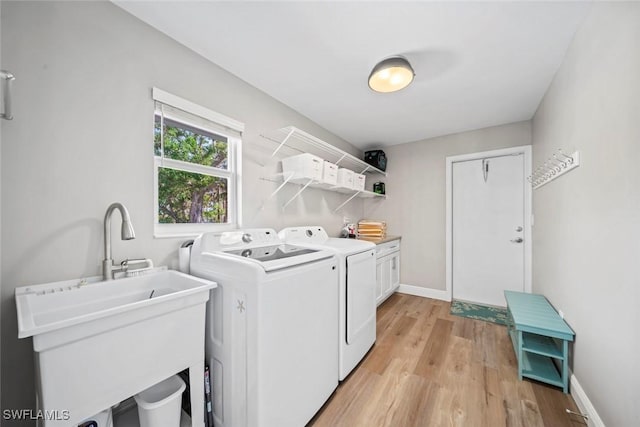 laundry room featuring light wood-type flooring, cabinet space, washing machine and dryer, and baseboards