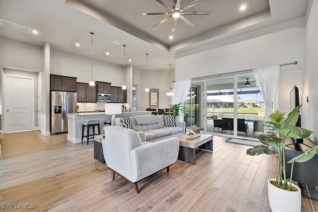 living room featuring ceiling fan, a high ceiling, and a tray ceiling