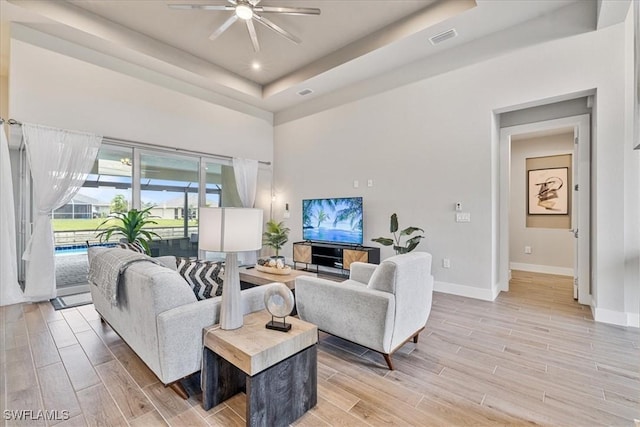 living room with a raised ceiling and ceiling fan