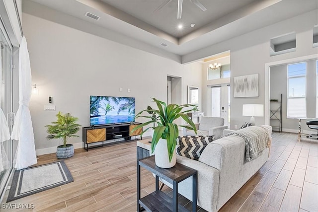 living room with ceiling fan with notable chandelier and a tray ceiling