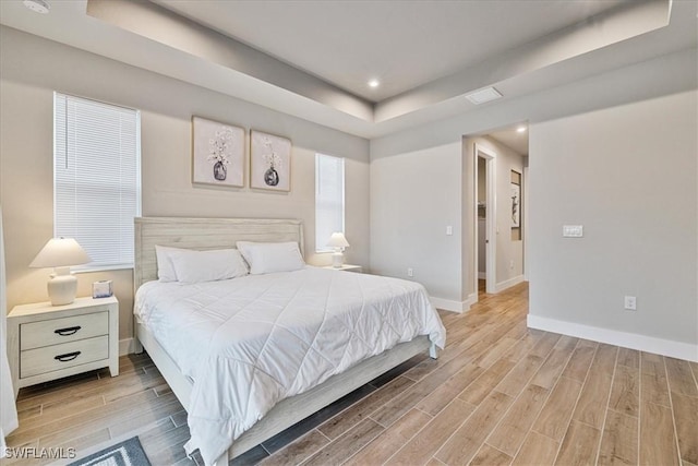 bedroom featuring a raised ceiling and light hardwood / wood-style flooring