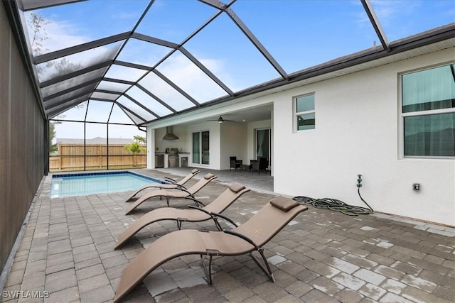 view of pool featuring a lanai, an outdoor kitchen, ceiling fan, and a patio area