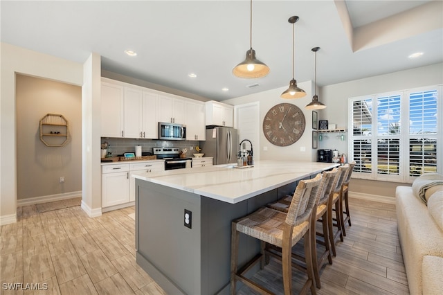 kitchen with light stone counters, a breakfast bar, stainless steel appliances, pendant lighting, and white cabinetry