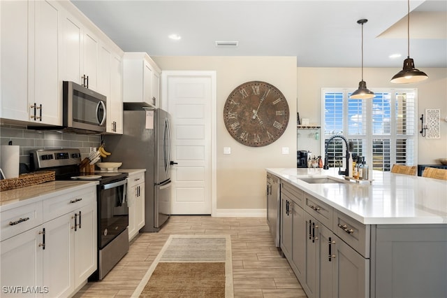 kitchen with gray cabinetry, stainless steel appliances, sink, decorative light fixtures, and white cabinets