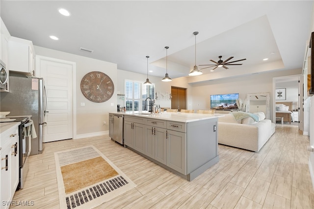 kitchen with appliances with stainless steel finishes, a raised ceiling, sink, a center island with sink, and white cabinets