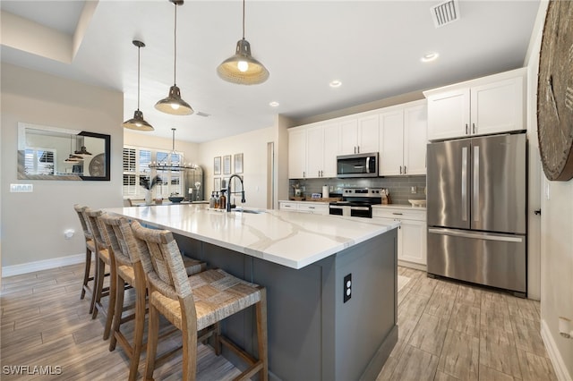 kitchen featuring light stone counters, a large island with sink, decorative light fixtures, white cabinets, and appliances with stainless steel finishes