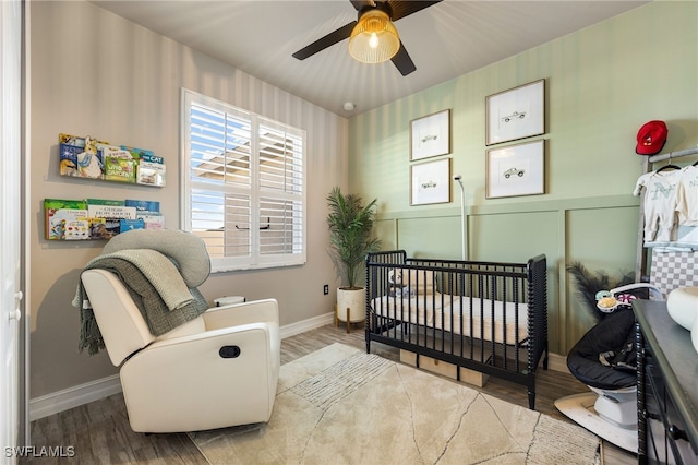 bedroom featuring ceiling fan, wood-type flooring, and a nursery area