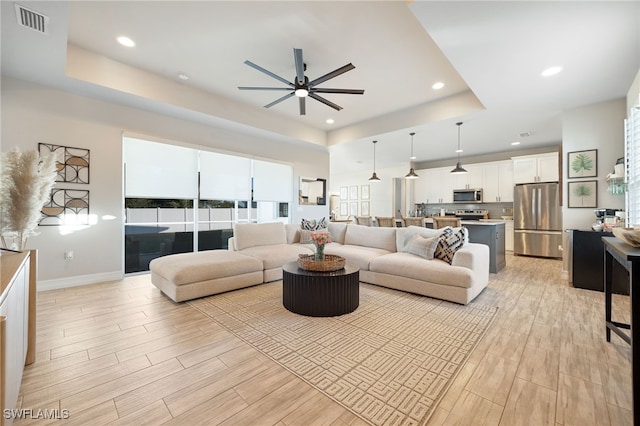 living room featuring ceiling fan and a raised ceiling