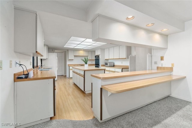 kitchen with a kitchen breakfast bar, sink, kitchen peninsula, black double oven, and white cabinetry