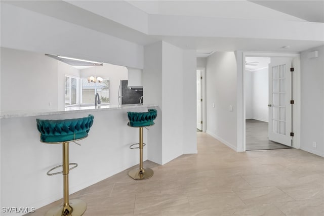 kitchen with a breakfast bar, sink, an inviting chandelier, stainless steel fridge, and white cabinets