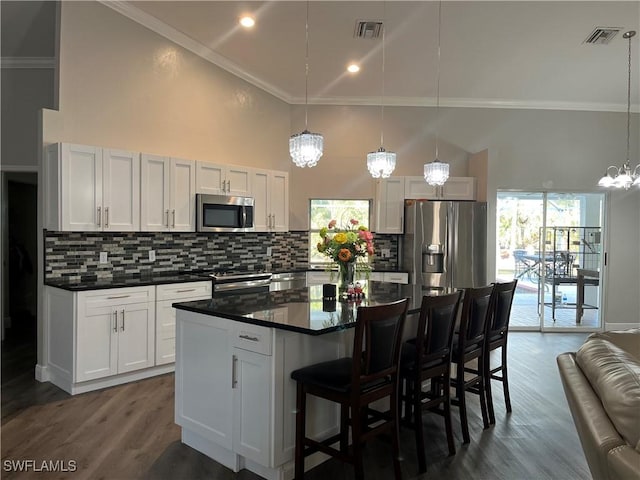 kitchen with appliances with stainless steel finishes, hanging light fixtures, a kitchen island, and white cabinets