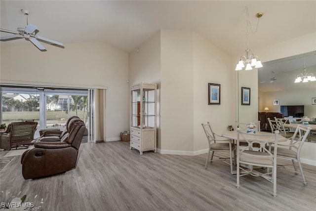 dining room with light wood-type flooring, ceiling fan with notable chandelier, and high vaulted ceiling