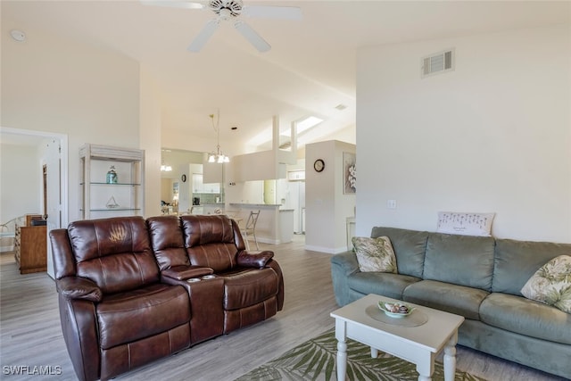 living room with ceiling fan with notable chandelier, light wood-type flooring, and lofted ceiling