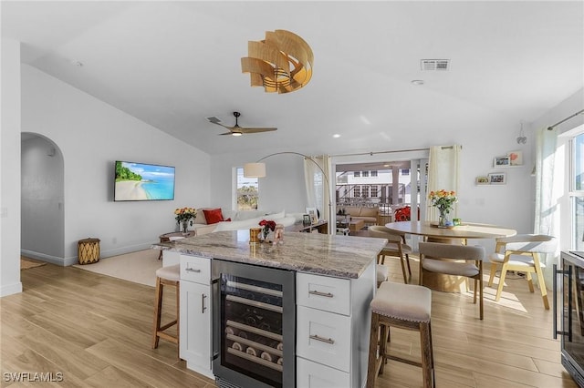 kitchen with lofted ceiling, white cabinetry, a kitchen breakfast bar, wine cooler, and light stone countertops