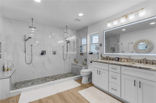 bathroom featuring a tile shower, vanity, wood-type flooring, and toilet