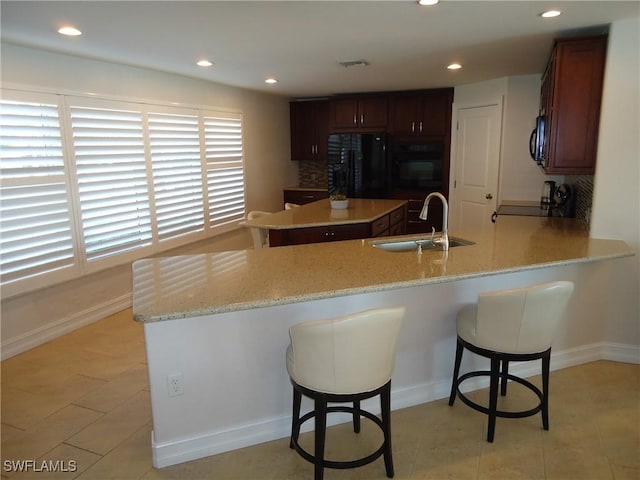 kitchen with black appliances, a kitchen breakfast bar, sink, decorative backsplash, and kitchen peninsula