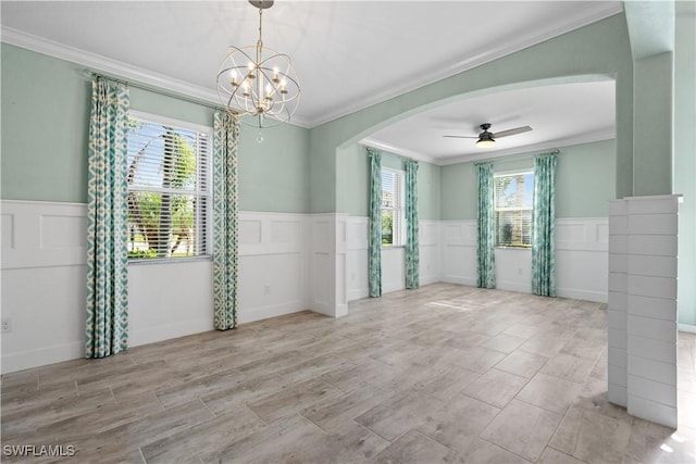 unfurnished room with a wainscoted wall, ceiling fan with notable chandelier, arched walkways, and ornamental molding