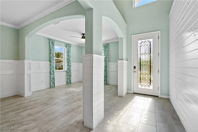 entryway with crown molding, a wainscoted wall, wood finished floors, arched walkways, and a ceiling fan