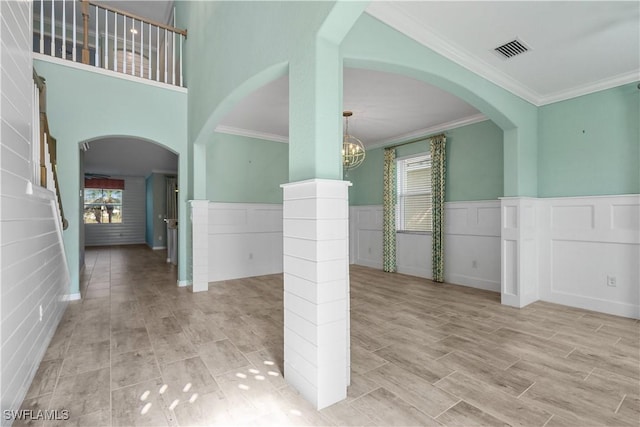 empty room with light wood-type flooring, decorative columns, crown molding, and a notable chandelier