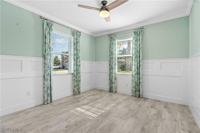 spare room featuring crown molding, a ceiling fan, and a wainscoted wall