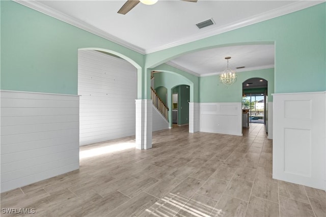 empty room with a wainscoted wall, ceiling fan with notable chandelier, crown molding, and visible vents