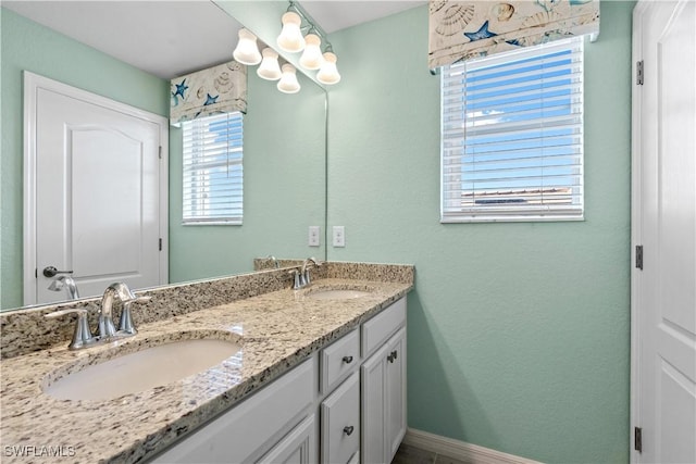 bathroom featuring double vanity, a notable chandelier, baseboards, and a sink