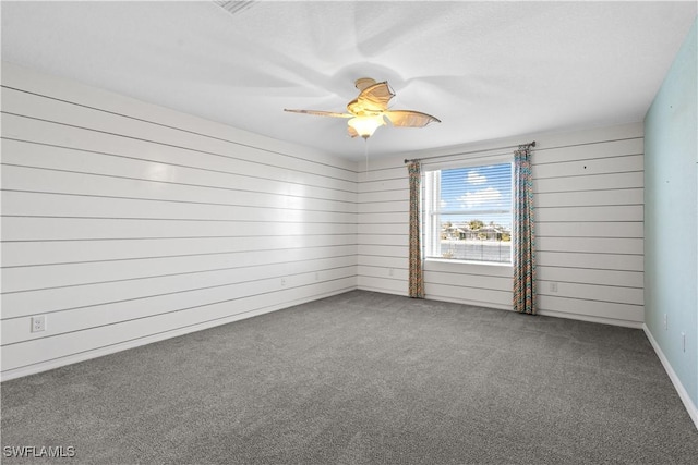 carpeted spare room with wood walls and ceiling fan