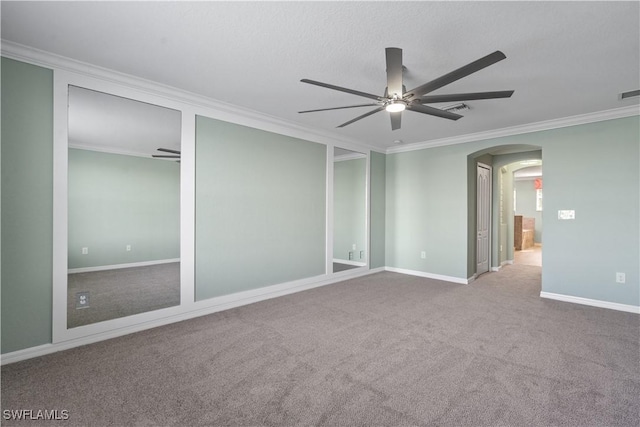 unfurnished room with crown molding, baseboards, ceiling fan, carpet floors, and arched walkways