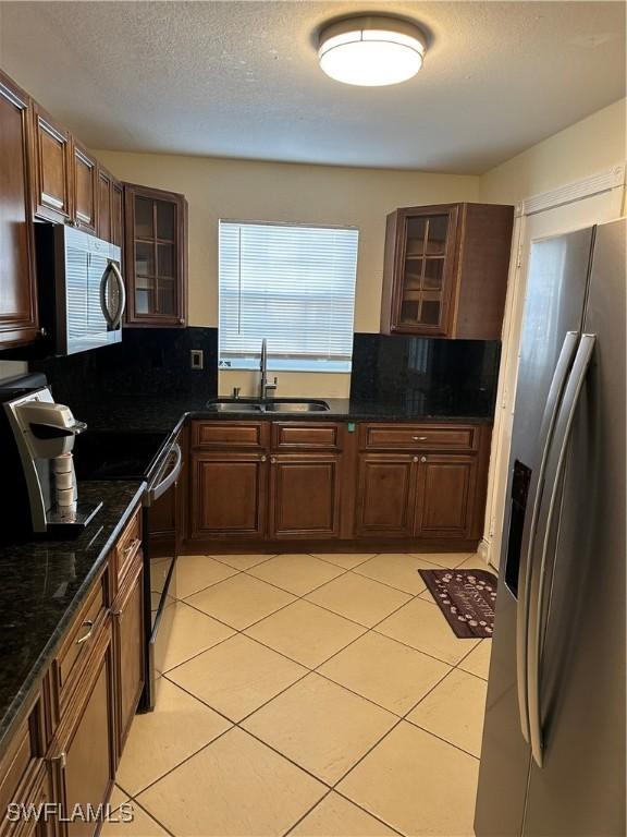 kitchen featuring tasteful backsplash, stainless steel appliances, sink, light tile patterned floors, and dark stone countertops