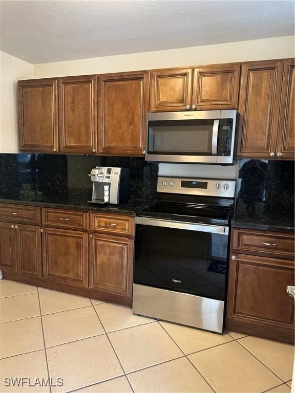 kitchen with decorative backsplash, light tile patterned flooring, dark stone countertops, and stainless steel appliances