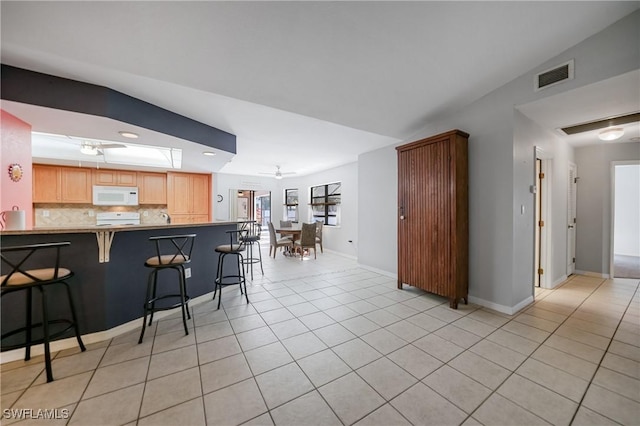 kitchen with ceiling fan, kitchen peninsula, lofted ceiling, decorative backsplash, and a breakfast bar