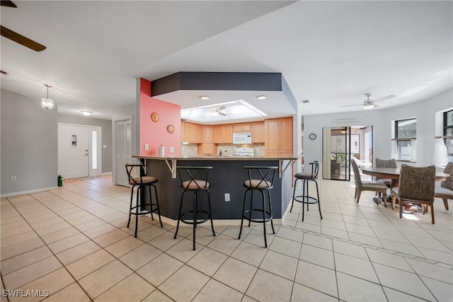 kitchen with light brown cabinets, ceiling fan, tasteful backsplash, kitchen peninsula, and a breakfast bar area