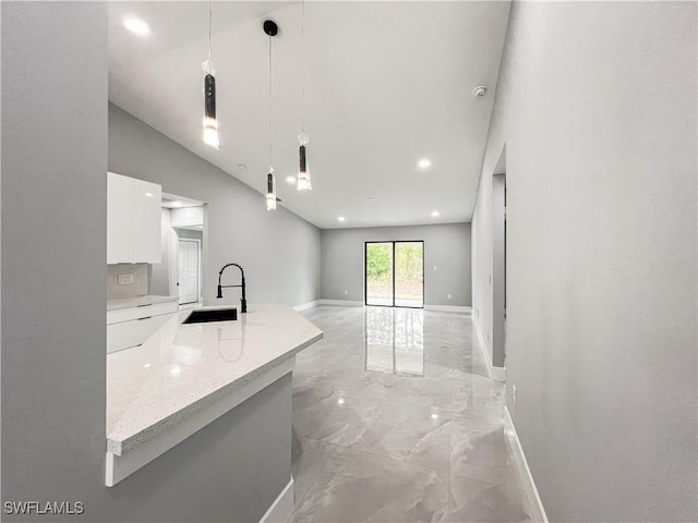 kitchen with light stone countertops, tasteful backsplash, sink, white cabinets, and hanging light fixtures