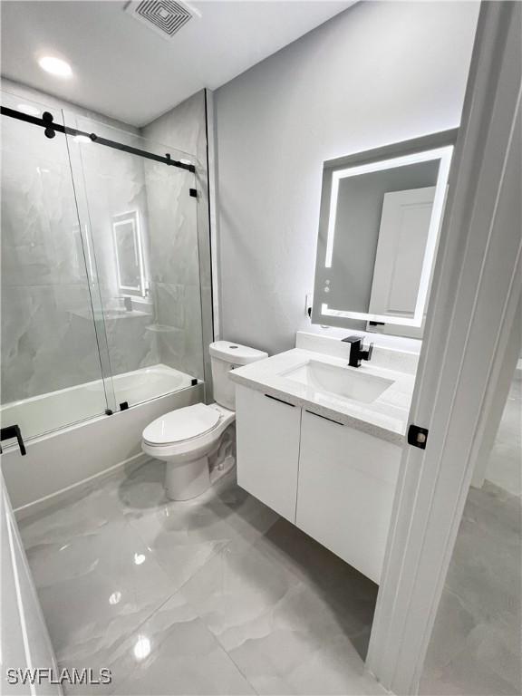 full bathroom featuring shower / bath combination with glass door, vanity, and toilet