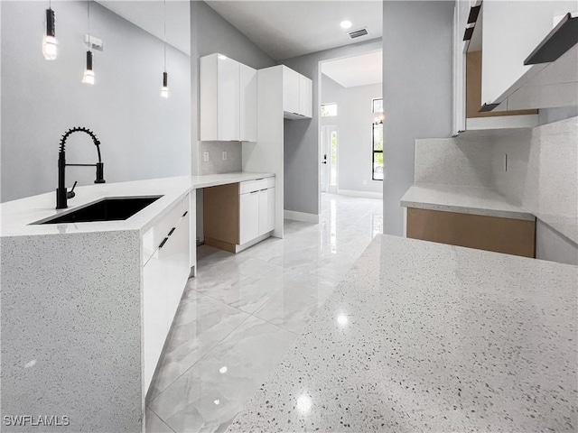 kitchen featuring pendant lighting, backsplash, white cabinetry, and sink