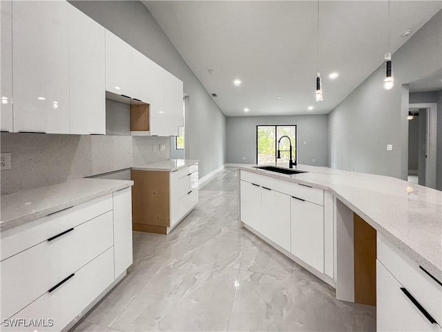 kitchen featuring sink, hanging light fixtures, tasteful backsplash, light stone counters, and white cabinetry