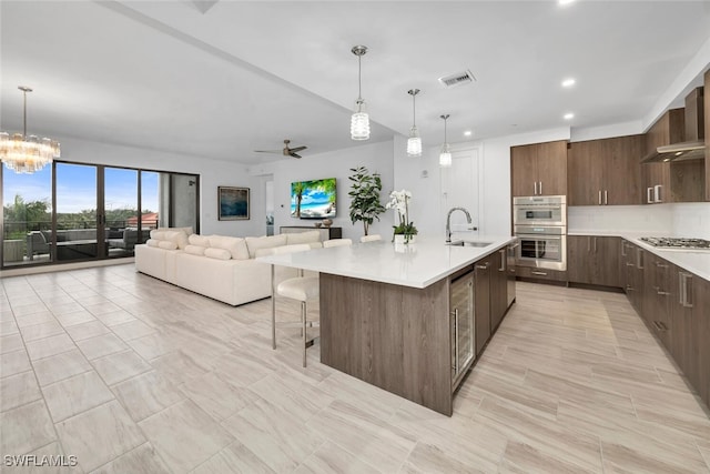 kitchen featuring decorative light fixtures, visible vents, open floor plan, light countertops, and a center island with sink