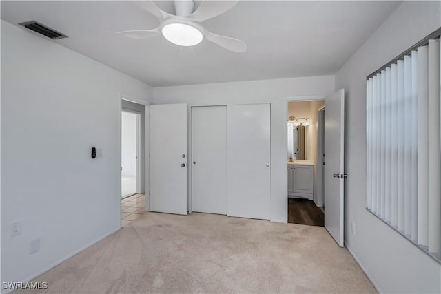 unfurnished bedroom featuring light carpet, a closet, ceiling fan, and ensuite bathroom