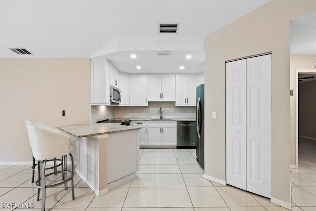 kitchen featuring white cabinetry, sink, stainless steel appliances, kitchen peninsula, and a kitchen bar