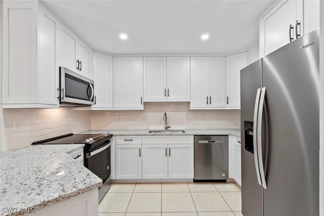 kitchen with appliances with stainless steel finishes, light stone counters, sink, light tile patterned floors, and white cabinets