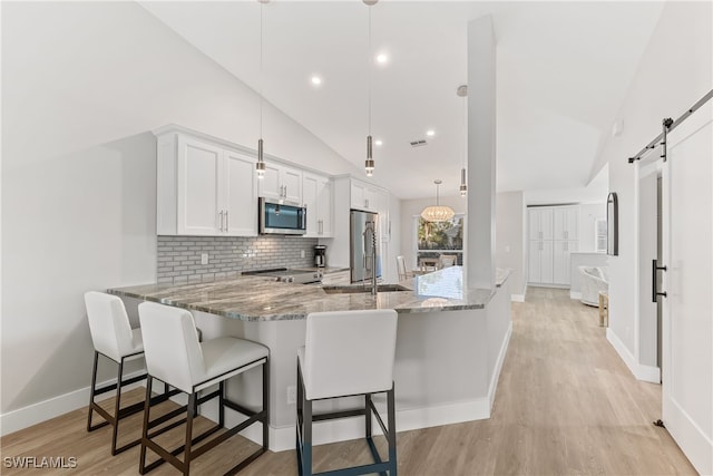 kitchen featuring appliances with stainless steel finishes, white cabinetry, hanging light fixtures, kitchen peninsula, and a barn door